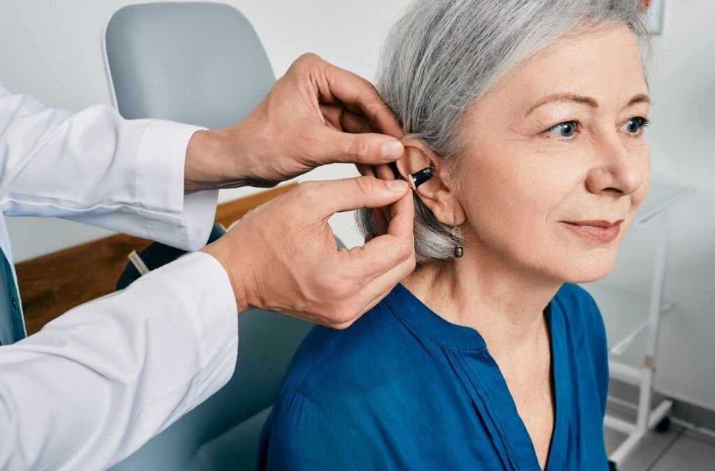 Senior woman during installation hearing aid into her ear by her audiologist.