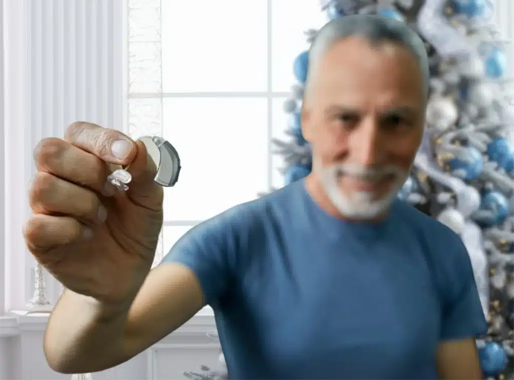 Man holding hearing aids in front of christmas tree